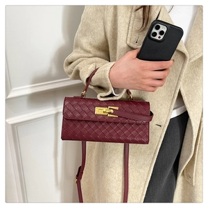Detail of burgundy woven leather texture with gold metallic lock on a crossbody bag