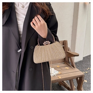 Detail of golden pleated evening clutch featuring a luxury crown rhinestone clasp and chain