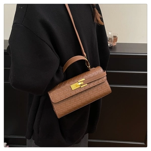 Dettaglio borsa Kelly marrone intrecciata con chiusura dorata su maglione nero di modella
