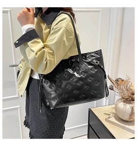 Detail of black glossy tote bag with embossed bow patterns and long tassel charm
