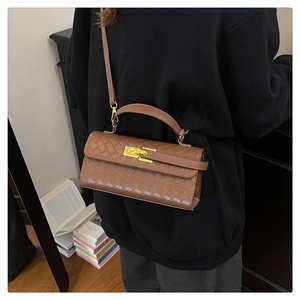 Close-up of brown woven leather texture and gold metal buckle on a stylish satchel bag