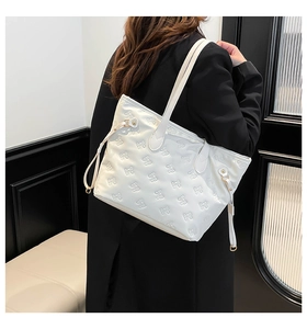 Shoulder view of white tote bag with embossed bow patterns and slender straps