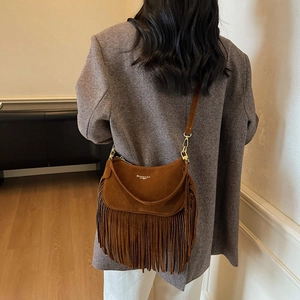 Dark brown suede crescent bag with fringe tassels worn by a model in a grey suit