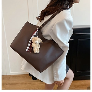 Détail du cabas en cuir mat marron foncé avec charm d'ours en peluche et écharpe rayée