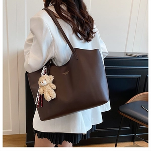 Sac cabas marron foncé avec charm ours en peluche porté par un mannequin en blazer