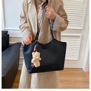 Détail d'un sac cabas en cuir noir avec un charm ours beige et un foulard en soie à carreaux