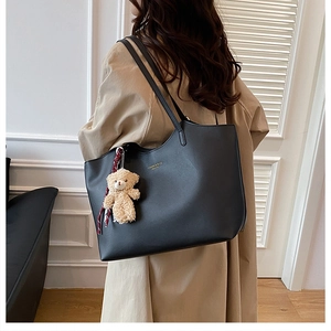 Détail d'un grand cabas en cuir noir avec un charm ours porté sur un trench-coat