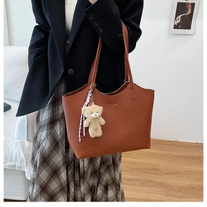 Détail d'un sac cabas caramel avec une breloque d'ours en peluche et logo doré gravé