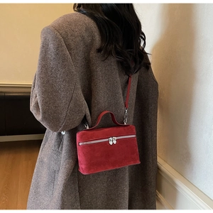 Detail of red suede mini bag with heart zippers worn over a stylish dark coat