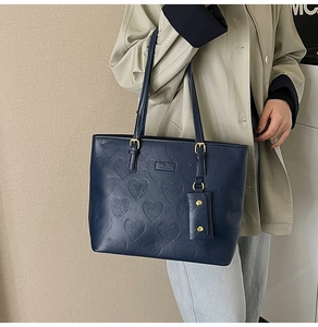 Détail d'un sac cabas bleu marine gaufré de cœurs avec ferrures dorées sur un trench-coat