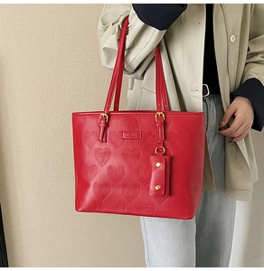 Grand sac cabas rouge avec gaufrage cœur et détails dorés porté par un mannequin
