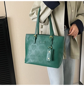 Détail du sac cabas vert avec gaufrage cœur et mini pochette porté par un mannequin