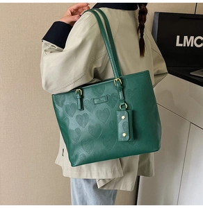 Détail du sac cabas vert foncé en cuir gaufré de cœurs porté par le mannequin