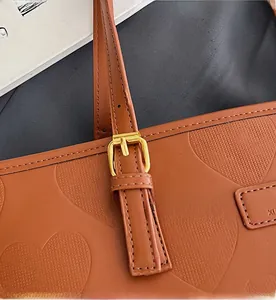 Détail d'un sac cabas en cuir marron avec gaufrage en cœur et boucle dorée
