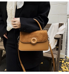 Close-up of brown suede and leather patchwork bag held on a bench with autumn leaves