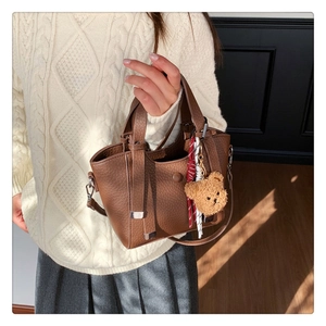 Detail of brown lychee grain leather handbag with cute plush bear charm and strap