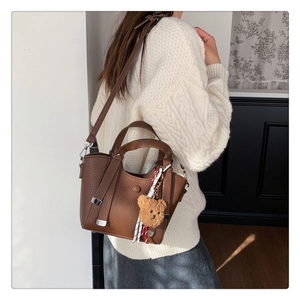 Detailed texture of brown pebble leather handbag with a plush bear charm accessory