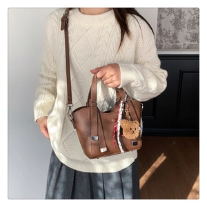 Close-up of brown litchi textured handbag with plush bear charm and striped ribbon