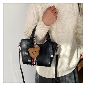 Detailed shot of black lychee grain leather handbag with cute bear charm and shoulder strap