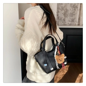 Detail of black lychee grain leather bag with plush bear charm and checkered ribbon decor