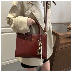 Détail du sac à main bordeaux en cuir brillant avec lettrage doré et accessoire créatif