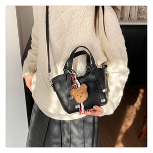 Close-up of small black lychee pattern leather handbag with brown plush bear charm detail