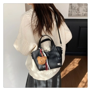 Rear view of a model carrying the black lychee pattern leather tote bag with teddy charm