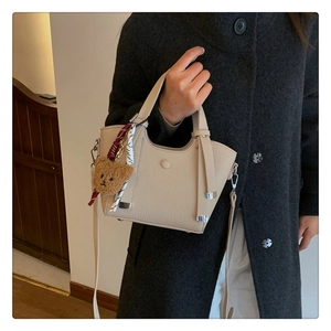 Detail of beige lychee leather handbag with plush bear charm on grey wool coat
