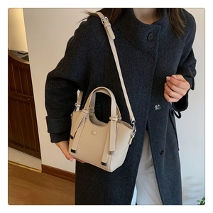Detail of a beige pebbled leather handbag with dual handles and metal reinforced corners