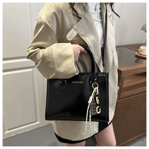 Détail d'un grand sac noir avec lettrage doré et chaîne sur un trench-coat beige