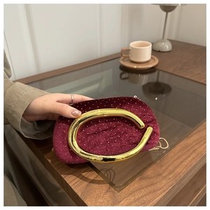 Close-up of burgundy velvet evening clutch with sparkling crystals and C-shaped gold handle