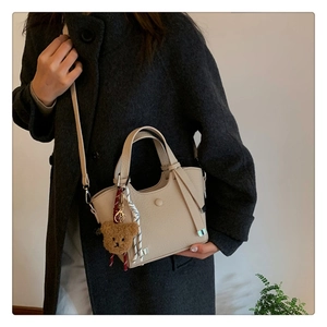 Detail of beige lychee grain leather handbag with cute bear charm and striped ribbon