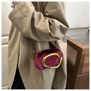 Detail of burgundy velvet clutch bag with gold C-shaped buckle on camel trench coat