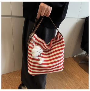 Gros plan du sac en toile rayé rouge et blanc avec bandoulière en cuir brun et pendentif