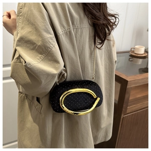 Detail of black velvet clutch featuring large gold oval handle and fine chain strap