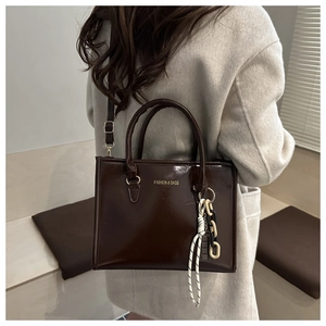 Détail du sac cabas marron brillant avec pendentif porté sur un manteau beige