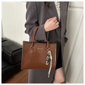 Gros plan du sac cabas marron en similicuir avec lettrage doré et chaîne décorative