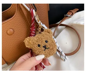 Detailed view of plush brown bear charm with red and white woven rope on a handbag