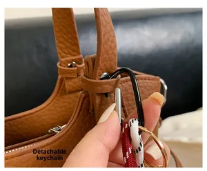 Detail of brown litchi leather handbag showing detachable woven rope charm on D-ring