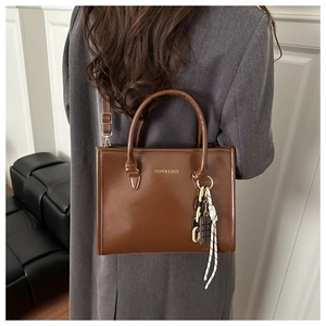 Détail du sac bandoulière en cuir marron brillant avec chaîne et accessoire corde