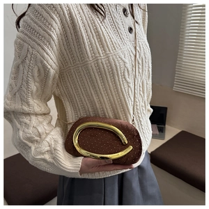 Detail of a brown velvet clutch with gold studs and a large semi-circular metal buckle