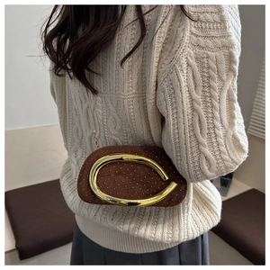 Detail of a brown velvet clutch bag with gold studs and C-shaped buckle worn by a model