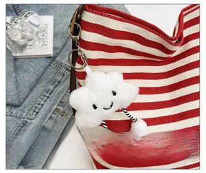 Detail of a white plush cloud charm with striped legs hanging on a striped canvas bag