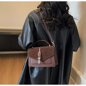 Detail of vintage brown shoulder bag showing suede flap and gold buckle on a model
