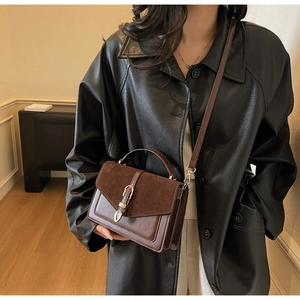 Detail of a brown vintage leather flap bag with gold buckle on a model in a black leather jacket