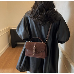 Brown crossbody bag with suede texture and metal buckle detail shown on shoulder