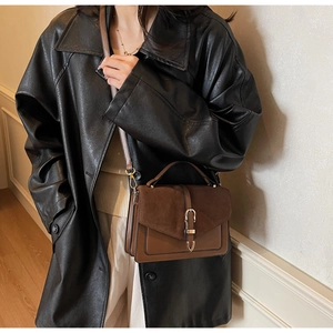 Detailed side view of a brown leather crossbody bag with U-shaped gold buckle on a model