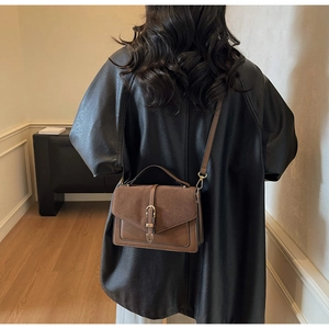 Detail of dark brown crossbody bag with suede flap and vintage golden U-shaped buckle lock