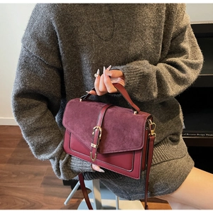 Detail of burgundy crossbody bag with leather mix texture and golden metal buckle