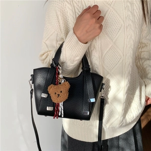 Fashionable black pebbled leather handbag with cute plush bear charm on white sweater model